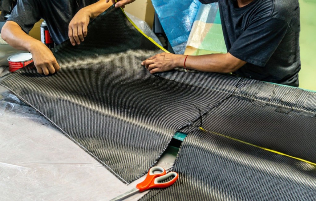 Workers handling a large sheet of carbon fiber fabric in a workshop